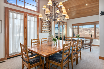 A dining room with a large wooden table and chairs, a chandelier, and a view of the mountains through a large window.
