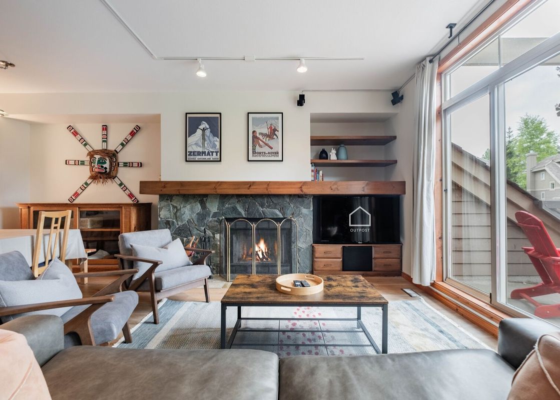 Cozy living room in Englewood Greens 14 featuring a stone fireplace, gray armchairs, and sliding glass doors to a balcony.