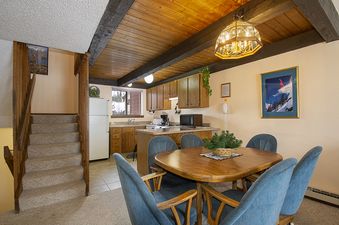 A dining table with blue chairs and a fully equipped kitchen with wooden cabinets and a white refrigerator.