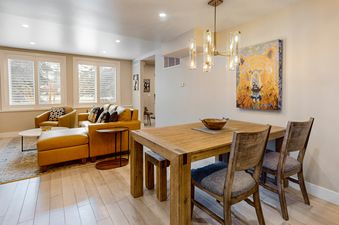 An inviting open-concept living area at Meadows Oxford 13 features a comfortable leather sectional and a wooden dining table beneath a stylish chandelier.