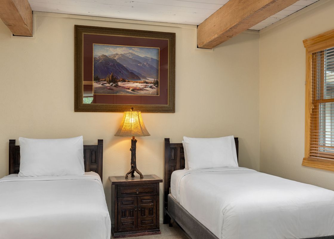 A cozy secondary bedroom at Top of the Village Slope 203 with two twin beds, a rustic lamp on a nightstand, and a mountain painting on the wall.