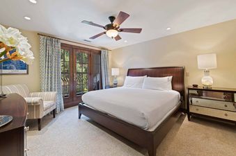 A king-sized bed with a dark wooden headboard and white bedding dominates the bedroom, flanked by a mirrored dresser and a patterned armchair.
