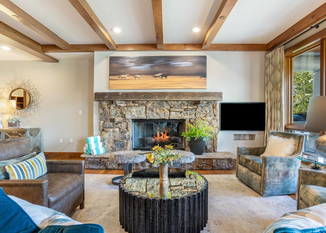 Cozy living room at 304C Bear Paw Lodge featuring a grand stone fireplace, wooden ceiling beams, and comfortable stylish seating.