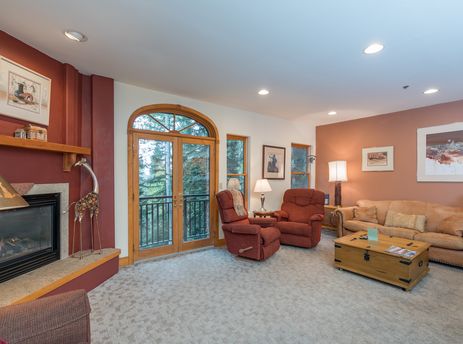 Bear Creek Lodge 302's living room has a fireplace, two armchairs, a couch, a coffee table, and a large window overlooking the forest.