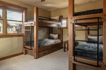 A cozy bunk room in Essentia Townhome 145A features custom wooden bunk beds with forest-themed bedding and bright windows.