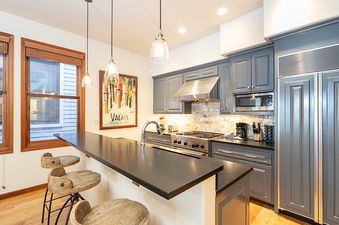 A kitchen with a breakfast bar and a view of the outside from two windows