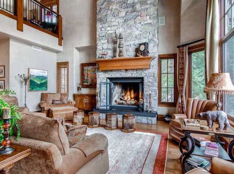 A spacious and elegantly furnished great room in Village Walk 55 features a large stone fireplace, comfortable seating, and expansive windows with outdoor views.