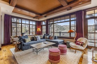 A cozy living room featuring a large sectional sofa, wooden coffee table, and an armchair, with expansive windows showcasing a mountain view.
