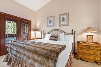A cozy bedroom at The Charter D4705 featuring a bed with a faux fur throw, traditional nightstands with lamps, and decorative stained-glass windows overlooking an outdoor scene.
