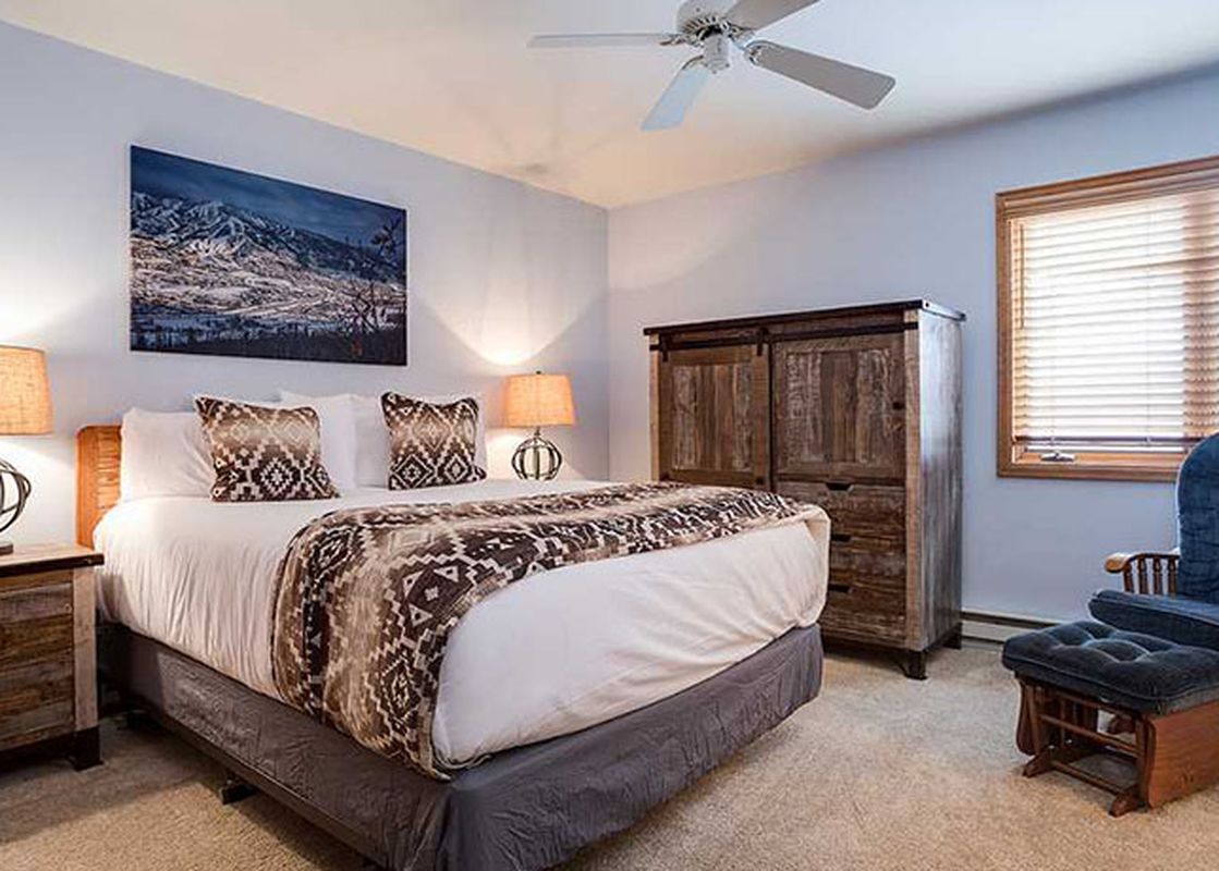 The king bedroom features a comfortable bed with rustic furnishings and a cozy armchair, ideal for relaxation at Pines Condominiums Two Bedroom.