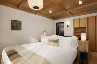 The serene king-sized bed in the Mollie Aspen Mountain Connecting Rooms bedroom features white linens and a striped throw, complemented by a natural wood ceiling and a built-in cabinet.