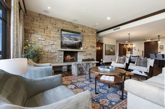 A cozy living room at Arrowleaf Lodge 415 features a stone fireplace, a large TV, plush seating, and a colorful rug, creating an inviting atmosphere for guests.