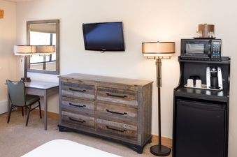 A hotel room at Beaver Run Resort featuring a wooden dresser, mounted flat-screen TV, desk with a chair, and a refreshment station with a microwave, coffee maker, and mini-fridge.