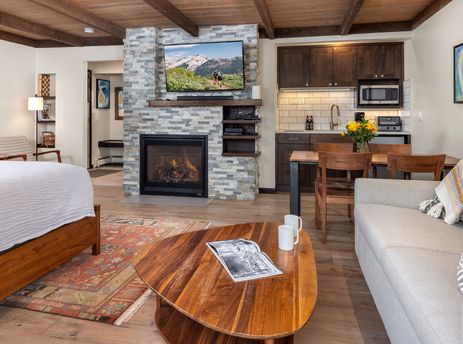 A wide shot of Willows C3 living room, kitchen, and bedroom with a comfortable sofa, a bed with white bedding, and a large fireplace.