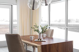 A modern dining room in Penthouse on Glenwood 407 features a live-edge wooden table, spherical glass pendant lights, and large windows with a snowy view.