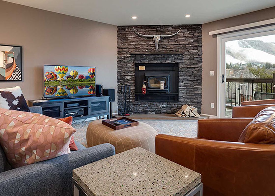 A cozy and well-appointed living room at Ranch at Steamboat RA511, featuring a stone fireplace, comfortable seating, and a large window with a view of a snowy mountain.