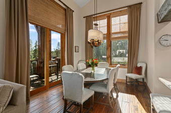 The dining area of Grand Lodge Five Bedroom Penthouse 406 features a wooden table with six chairs, a large window with a view of the mountains, and a chandelier.