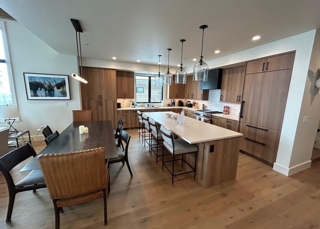 The dining room features a long wooden table with leather chairs and a view of the kitchen.