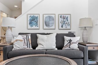 A cozy living room with a dark gray sofa, ski-themed throw pillows, abstract art, and two decorative table lamps.