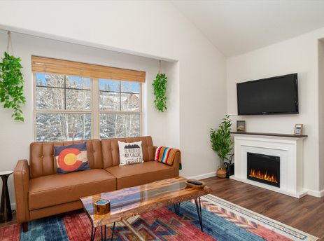 The living room at Waterside West A303 features a comfortable leather sofa, a modern fireplace, and a large window overlooking a snowy landscape.