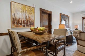 A rustic dining area with a wooden table, leather and upholstered chairs, and a painting of birch trees on the wall.