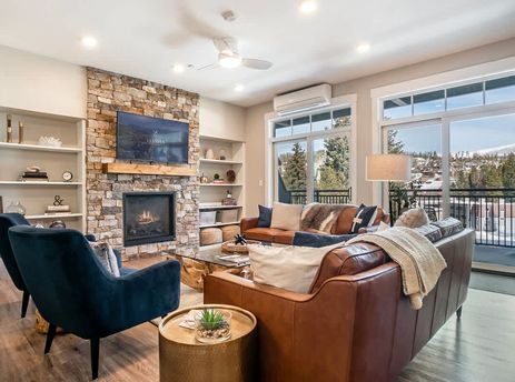 The inviting living area of Hideaway Haven features a stone fireplace, comfortable brown leather sofas, and large glass doors that open to a balcony with scenic views.