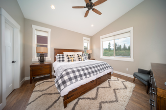 A spacious bedroom at Alder Brook Homers Hideaway features a large bed with checkered bedding, wooden furniture, and bright windows with views of the outdoors.