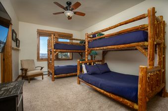 A rustic bunk room at EagleRidge Townhomes 1461 with two wooden bunk beds, navy blue bedding, a window with a scenic view, an armchair, and a ceiling fan.