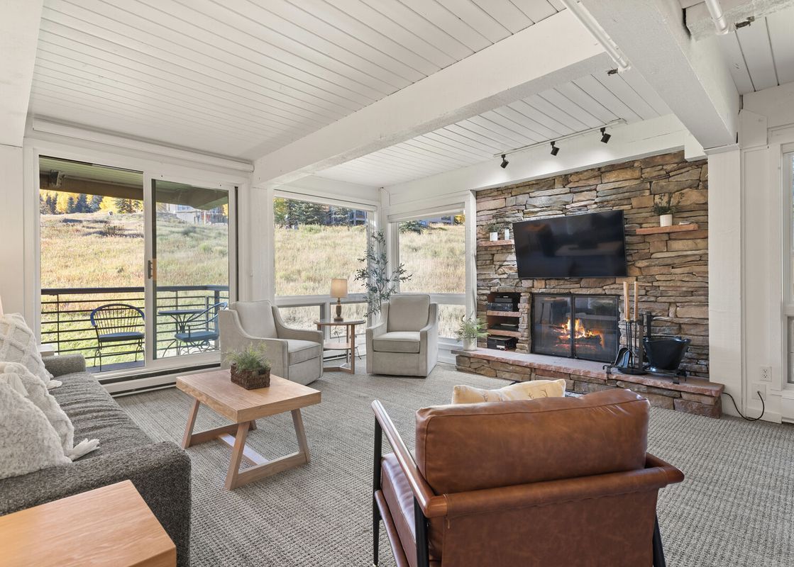 The spacious living room at Enclave 209 features comfortable seating, a stone fireplace with a TV, and large windows with scenic outdoor views.