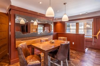 A cozy dining area at Cedar Crest Robin Cottage 6 features a rustic wooden table with four leather chairs, set against warm reddish-brown paneled walls and chevron-patterned wooden flooring.
