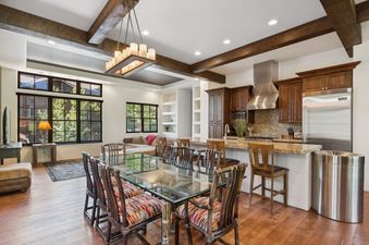A modern rustic dining room with a glass table and colorful chairs, next to a kitchen with dark wood cabinets and stainless steel appliances.