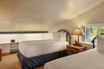 A cozy bedroom in Vantage Point 503 features two twin beds with white bedding, wrought iron headboards, a rustic wooden nightstand with a lamp, and a window showcasing green trees.