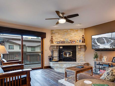 A cozy living room at Ranch at Steamboat RA401 with a stone fireplace, flat-screen TV, and balcony access.
