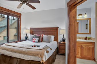 A primary bedroom at Crystal Peak Lodge 7407 featuring a king-sized bed with an ornate wooden headboard and an adjacent bathroom with a vanity and shower.