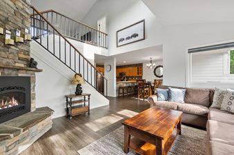 The Tee Time living room features a cozy fireplace, a comfortable L-shaped sofa, and a wooden coffee table, with a view into the kitchen and dining area.