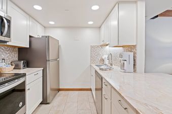A modern kitchen with white cabinets, stainless steel appliances, and a marble countertop.