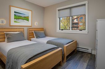 The bedroom at Ranch at Steamboat RA220, featuring two beds with white sheets and grey comforters, a light wooden headboard, a framed landscape picture, and a modern wall sconce.