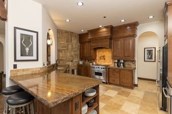 The kitchen at the Estate at Baldy Ridge boasts warm wood cabinetry, a granite island with seating, and stainless steel appliances.