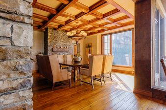 Dining area with a wooden table, high-backed chairs, a stone accent wall, and a coffered ceiling at The Developers Residence at See Forever.