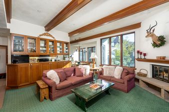 The living area features two comfortable sofas with plush pillows, a glass-top coffee table, and a fireplace, with a view into the kitchen and dining areas.