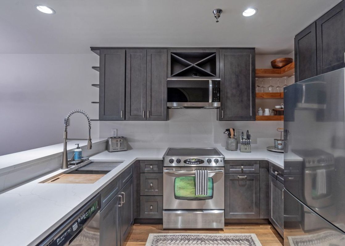 A modern kitchen with dark wood cabinets, stainless steel appliances, and a white countertop, featuring a sink, microwave, and stove.
