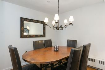 A formal dining area features an oval copper-top table surrounded by six dark brown leather chairs, illuminated by an elegant wrought iron chandelier.
