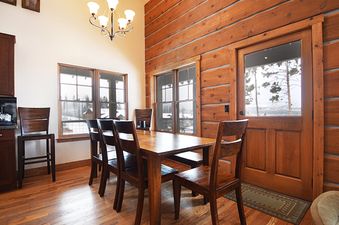 A dining area with a wooden table, chairs, and large windows overlooking a snowy landscape.