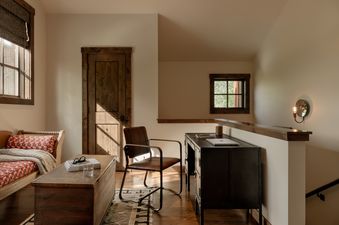 An inviting office nook in Four Pines 09 features a wooden desk, a brown leather chair, and a decorative bench, all bathed in natural light.