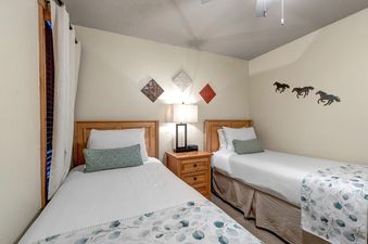 A peaceful twin bedroom at Snow Flower 132 Park City with two beds, a central nightstand, decorative wall art, and curtains by the window.
