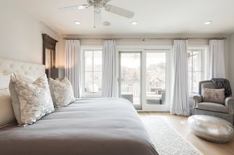 A bright and elegant master bedroom with a large bed, balcony access, and a cozy armchair.