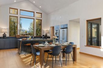 A spacious dining and kitchen area at Alpenglow Jackson Hole with a wooden table, dark cabinetry, and expansive windows showing mountain views.