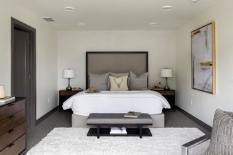 A cozy bedroom at Penthouse on Glenwood 401 featuring a king-sized bed, stylish nightstands with lamps, a decorative bench, and a modern art piece.