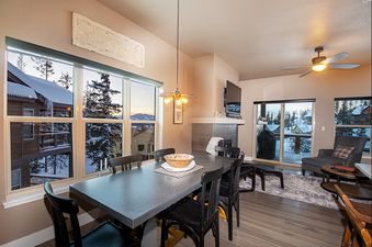 The dining area and living room of Rendezvous 47 Lookout Point are elegantly furnished, featuring large windows that offer a stunning view of a snow-covered landscape.