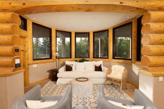 A cozy lounge area in the Modern Ski Home features a cream-colored sofa with throw pillows and two gray armchairs, all set on a patterned rug.